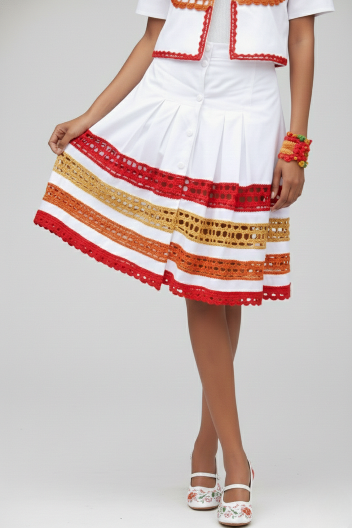 Falda Short Tribal blanca con pliegues frontales, botones y franjas de crochet rojo, naranja y beige en el ruedo | Claudia Bertolero