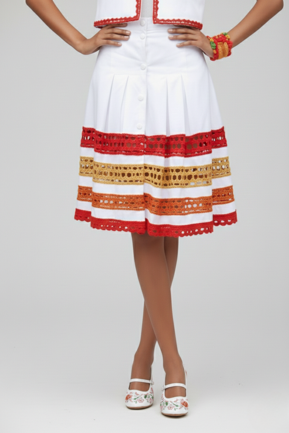 Falda Short Tribal blanca con pliegues frontales, botones y franjas de crochet rojo, naranja y beige en el ruedo | Claudia Bertolero
