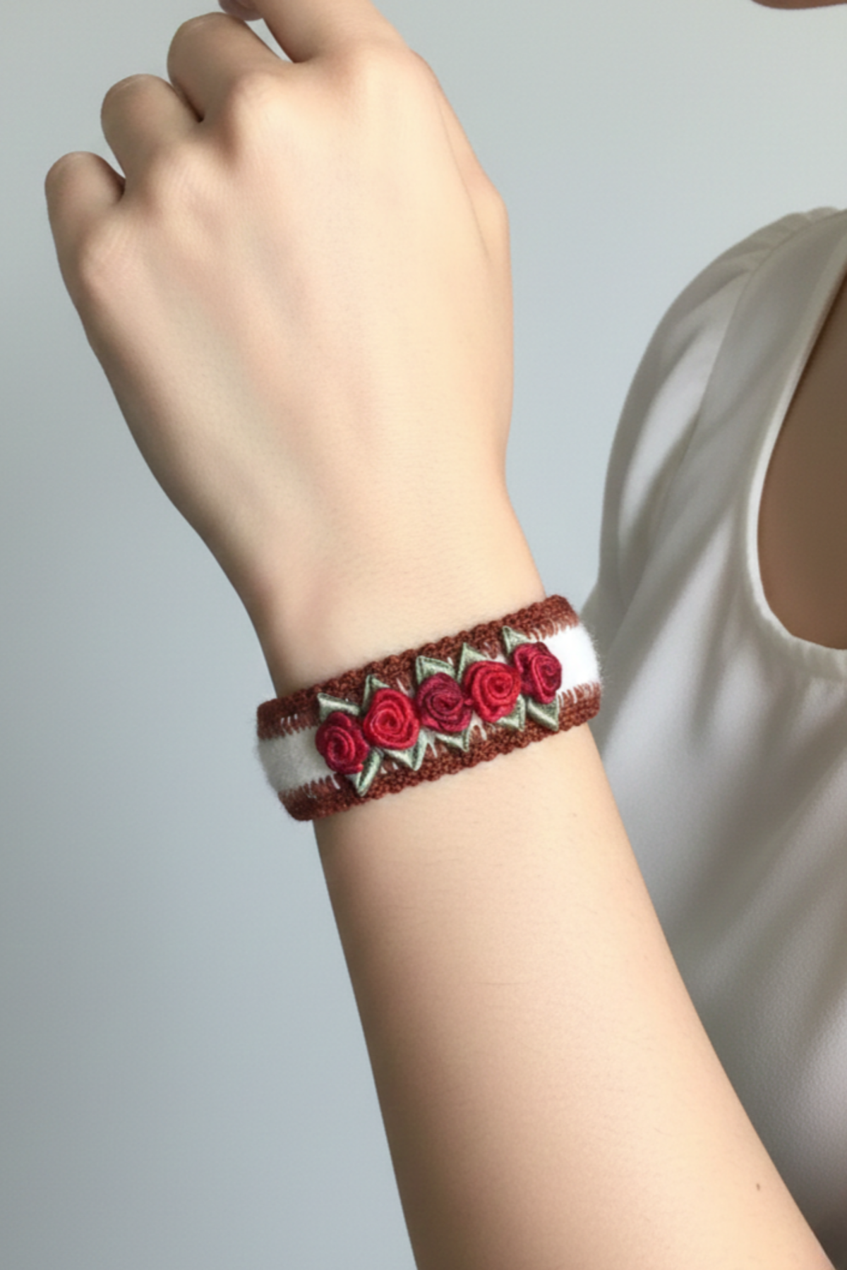 Brazalete Rosa artesanal con bordado a crochet y rosas de cintas satinadas rojas sobre base de alpaca, colocado en la muñeca mostrando su diseño floral y cierre metálico | Claudia Bertolero