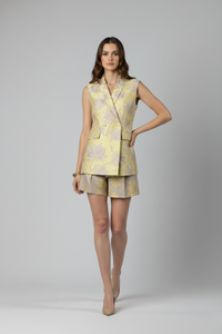 Modelo caminando con Chaqueta Del Rosario en brocado amarillo con relieve floral, diseño entallado con cruce asimétrico y botones forrados que aportan un estilo sofisticado | Claudia Bertolero