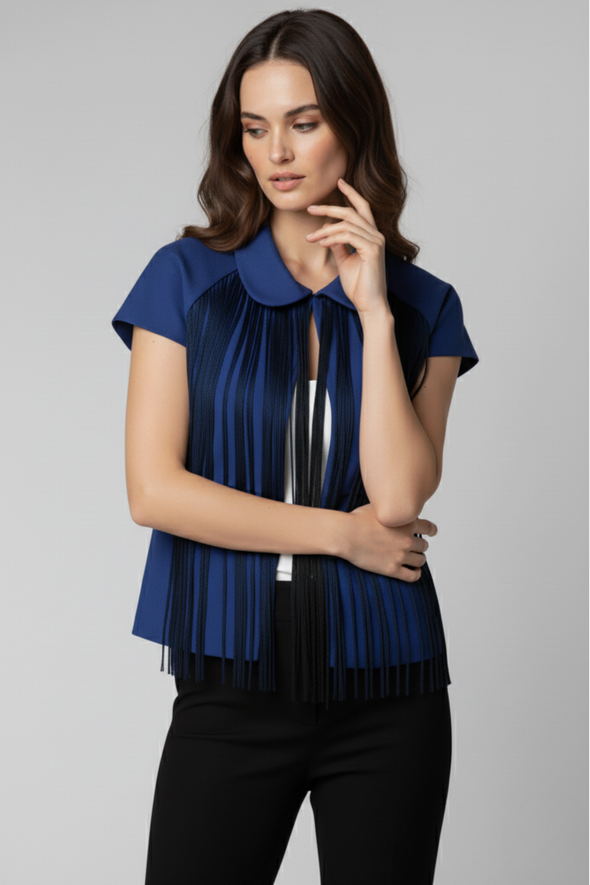 Modelo con bolero Batsheva azul de manga corta y cuello redondeado. Flecos largos en tonos oscuros recorren el frente, combinados con top blanco y pantalón negro | Claudia Bertolero