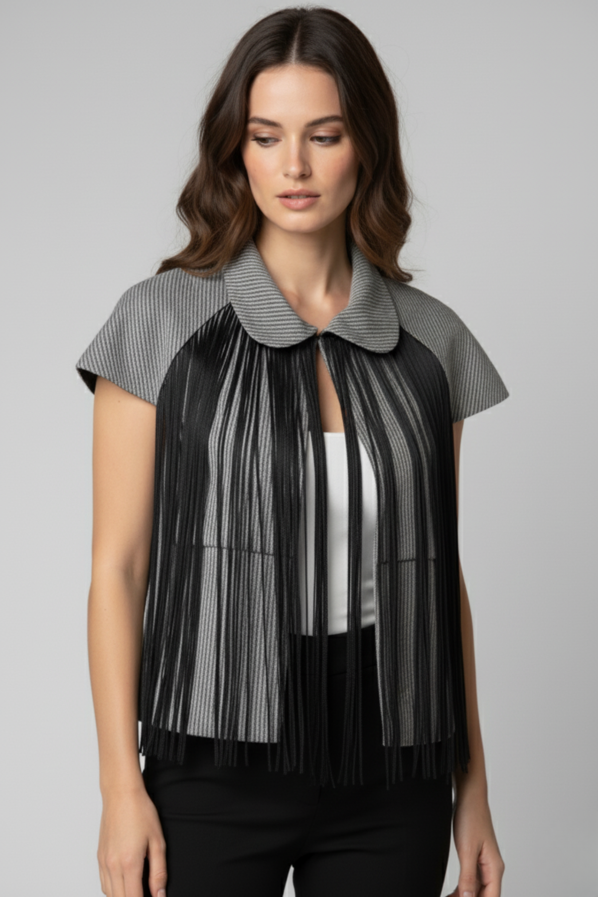 Modelo con bolero Batsheva gris de manga corta y cuello redondeado, con flecos largos negros que caen desde el frente sobre un top blanco y pantalón negro | Claudia Bertolero