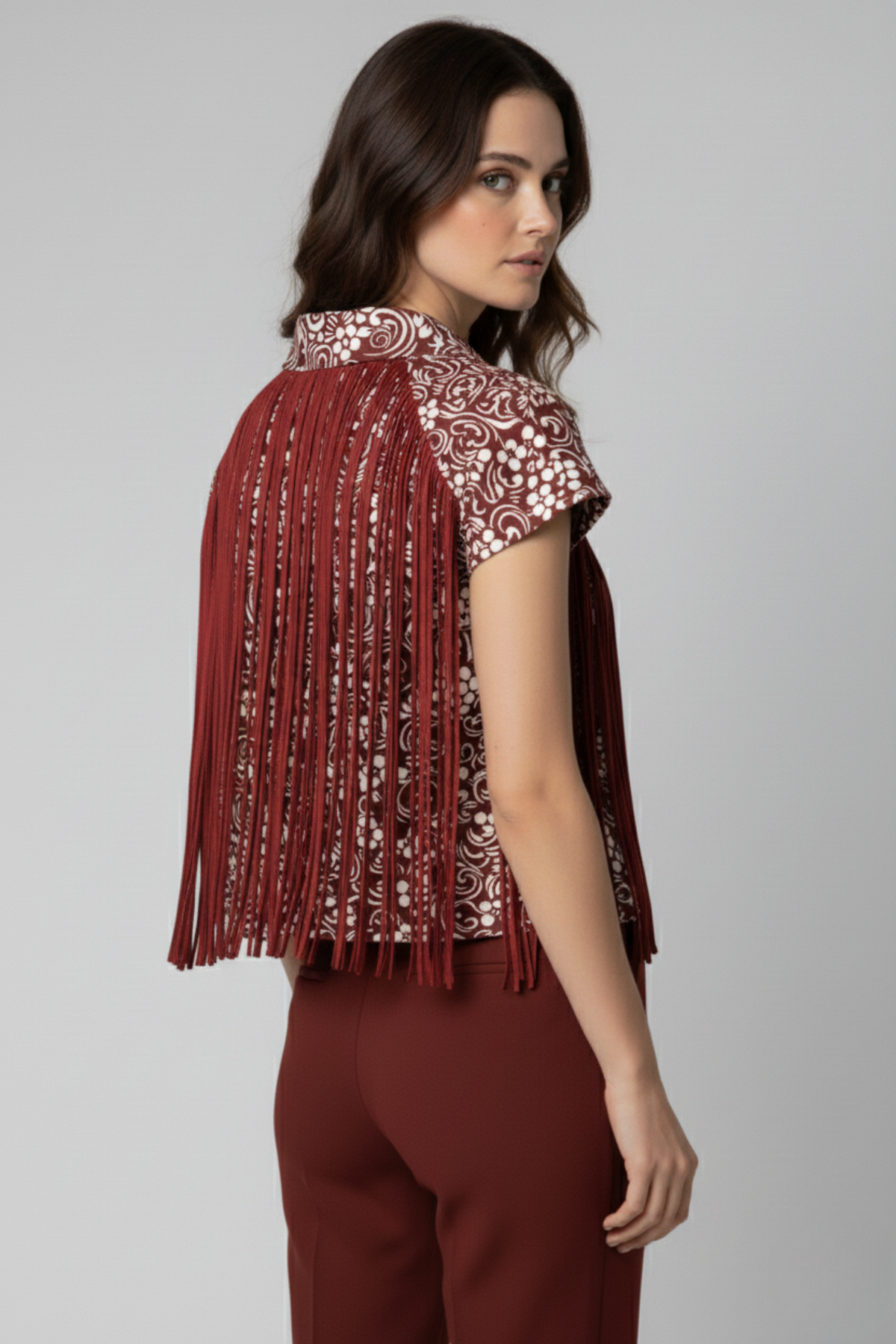 Vista posterior del bolero Batsheva rojo con estampado blanco. Los flecos largos de cintas satinadas cubren la espalda, creando movimiento y textura sobre el pantalón rojo | Claudia Bertolero