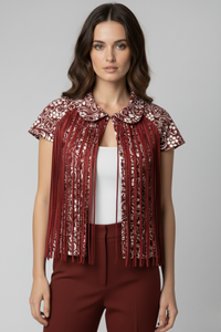 Modelo con bolero Batsheva rojo con estampado blanco, manga corta y cuello redondeado. El diseño presenta flecos largos de cintas satinadas en la parte frontal que caen sobre un top blanco y pantalón rojo | Claudia Bertolero