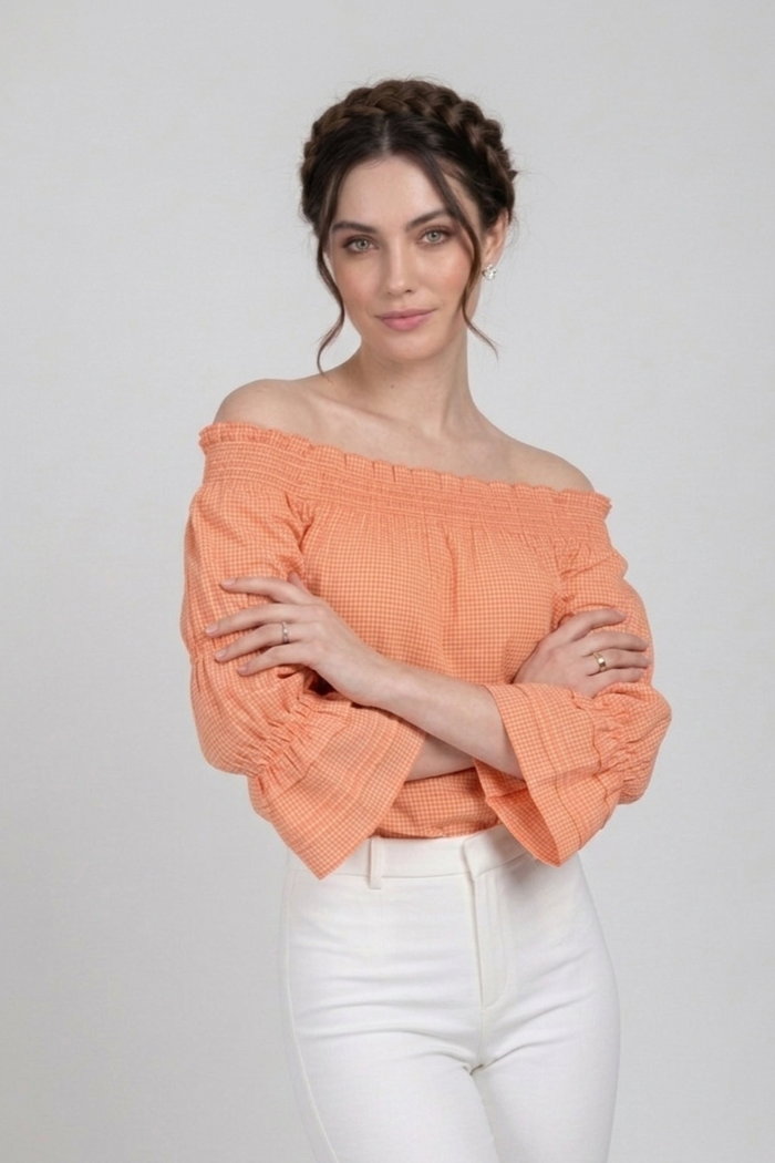 Blusa Penélope en tela vichy de algodón color durazno con diseño off shoulder y mangas largas con elástico. La modelo la combina con pantalón blanco, mostrando un look fresco y veraniego | Claudia Bertolero